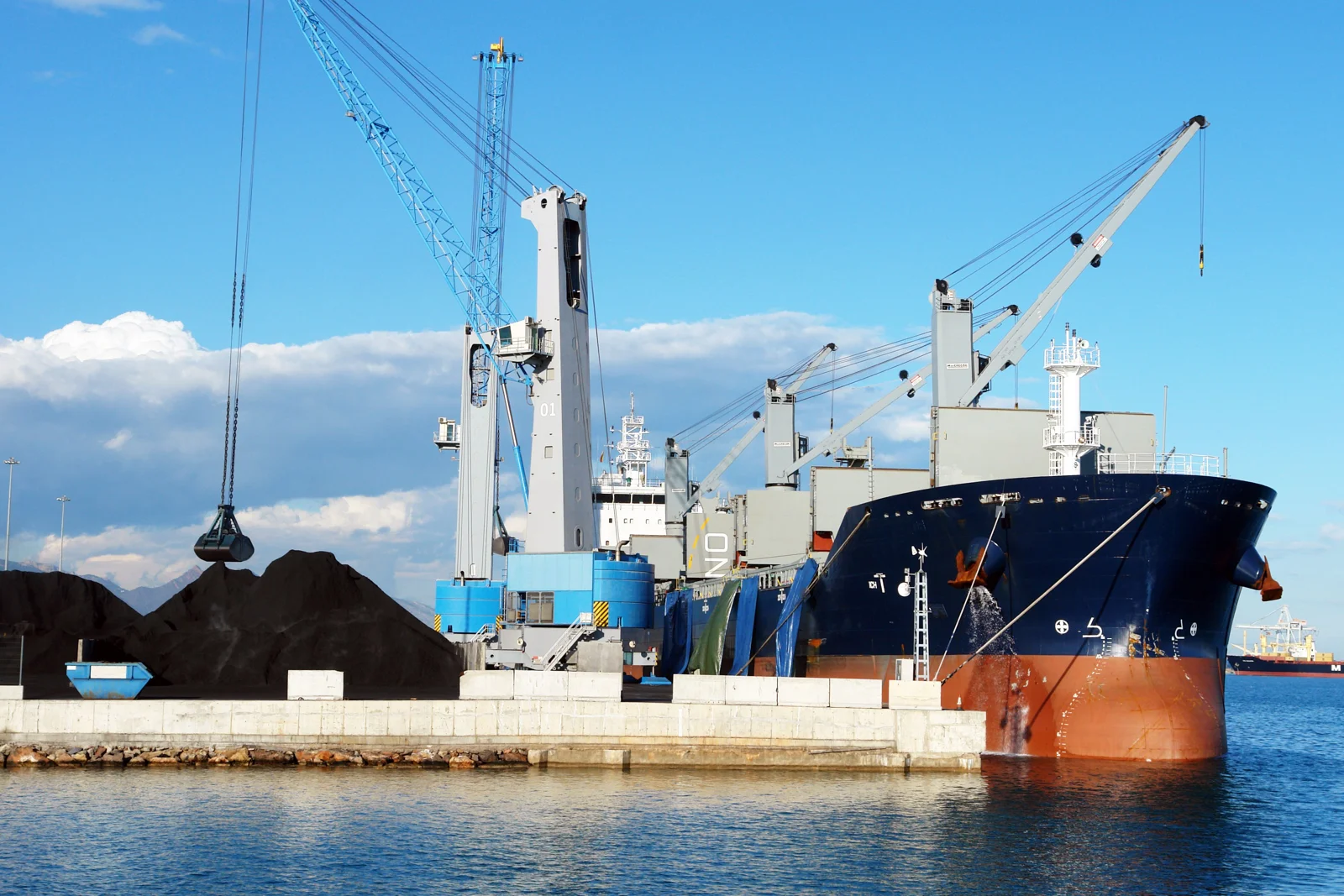 Bulk cargo vessel docked at an industrial port with loading cranes
